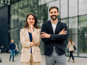 Eine Frau und ein Mann im Business Outfit blicken selbstbewusst in die Kamera.